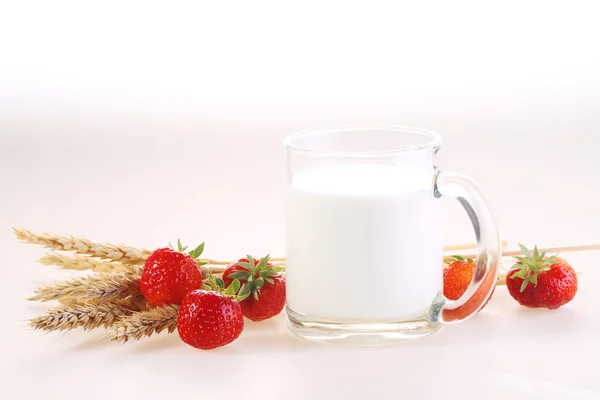 Leche en una taza transparente y una fresa fresca en una espalda blanca — Foto de Stock