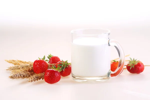 Leche en una taza transparente y una fresa fresca en una espalda blanca — Foto de Stock