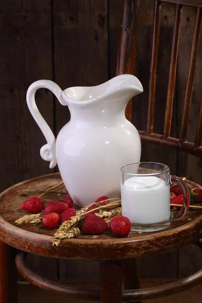 Milch in einem durchsichtigen Becher und eine reife Erdbeere auf einem Holztisch — Stockfoto