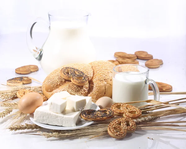 Natura morta con latte in una brocca trasparente, un rotolo e una brynza — Foto Stock