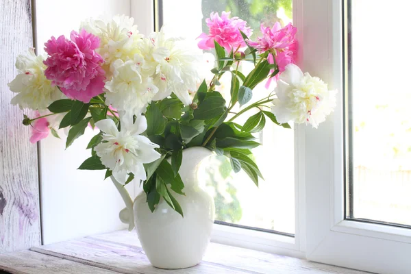 Bouquet de pivoines blanches et roses dans une cruche sur un rebord de fenêtre blanc — Photo