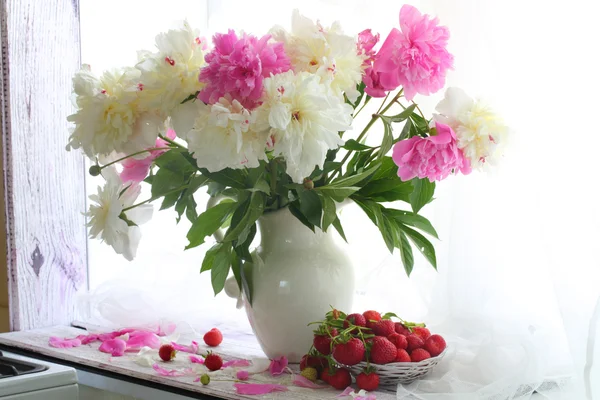 Strawberry in a wattled vase and a bouquet of peonies on a white — Stock Photo, Image