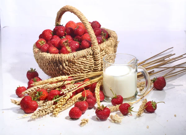 Fresa en una cesta de mimbre y leche en una taza transparente en — Foto de Stock