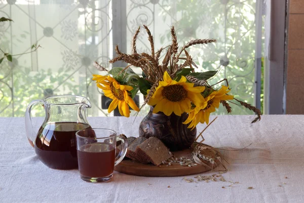 Stillleben mit Kvass (kvas) in einem transparenten Krug und einem Strauß — Stockfoto