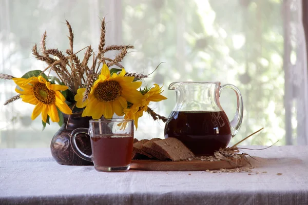kvass (kvas) in a transparent jug and a bouquet of sunflowers