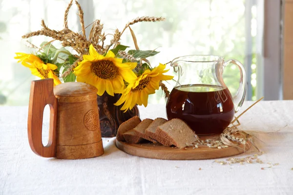 Kvass (kvas) en una jarra transparente, una taza de madera y un ramo de — Foto de Stock