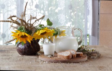 Süt şeffaf bir sürahi, ekmek ve ayçiçeği bir buket