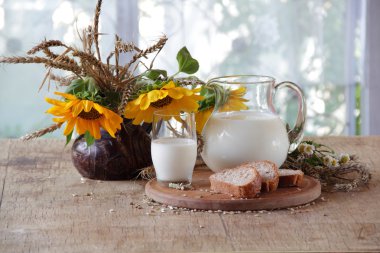 Süt şeffaf bir sürahi, ekmek ve ayçiçeği bir buket