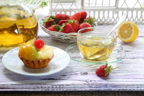 Cake with fruit and tea with a lemon in a transparent cup