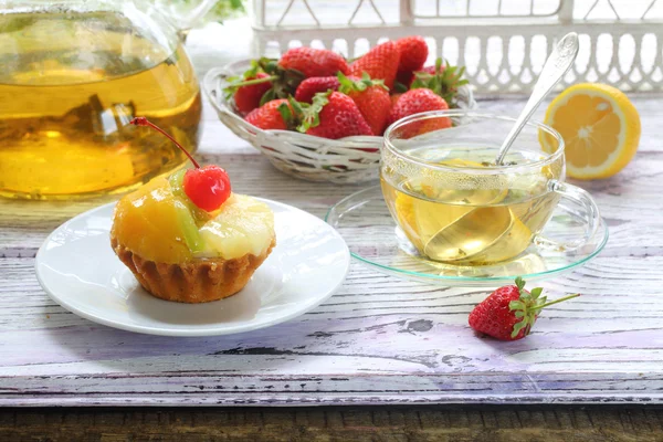Cake with fruit and tea with a lemon in a transparent cup