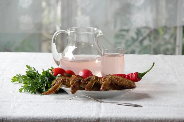 Chicken wings of a barbecue and compote in a transparent jug — Stock Photo, Image