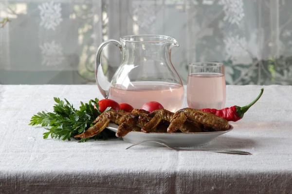 Chicken wings of a barbecue and compote in a transparent jug — Stock Photo, Image