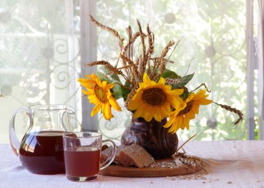 Kvas (kvas) şeffaf bir sürahi, ekmek ve bir buket sunflo