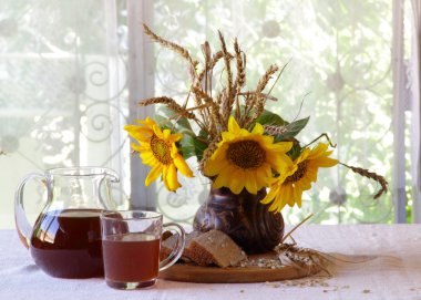 Kvas (kvas) şeffaf bir sürahi, ekmek ve bir buket sunflo