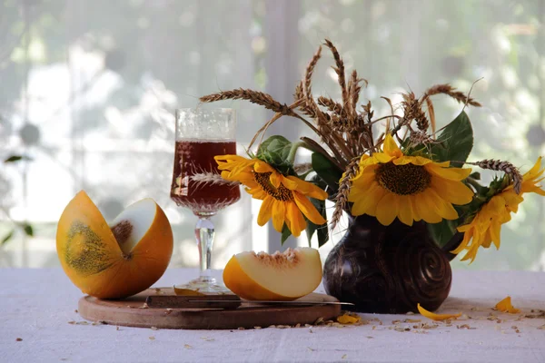 Vin rouge dans un beau verre, un melon mûr et un bouquet de soleil — Photo