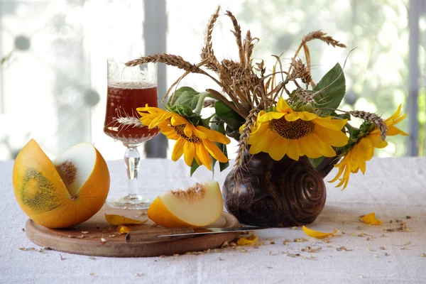 Vin rouge dans un beau verre, un melon mûr et un bouquet de soleil — Photo