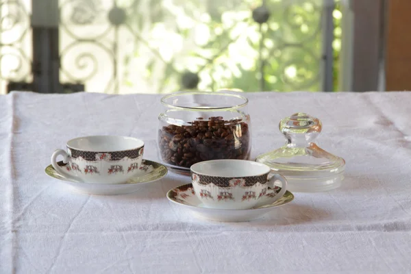 Pair of coffee cups and coffee grain in transparent bank — Stock Photo, Image