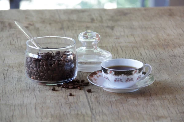 Grãos de café em banco transparente e uma xícara de café — Fotografia de Stock