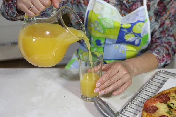 Женщина наливает апельсиновый сок из прозрачного кувшина — стоковое фото