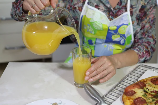 Женщина наливает апельсиновый сок из прозрачного кувшина — стоковое фото