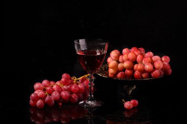 Cam ve pembe üzüm siyah bir zemin üzerine kırmızı şarap
