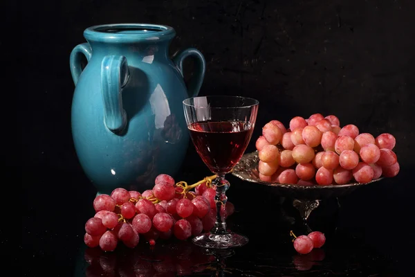 Vinho tinto e uvas rosa sobre um fundo preto — Fotografia de Stock