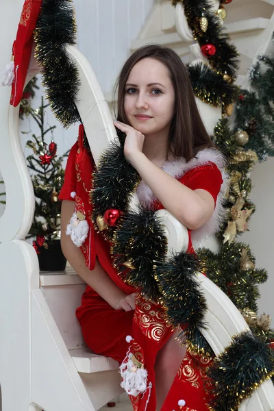 Девушка в костюме Санти на белой лестнице вокруг мехового дерева — стоковое фото