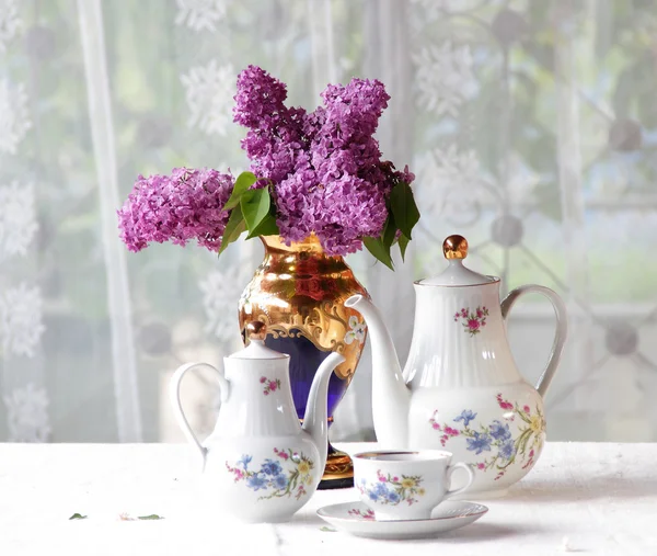 Té en una taza, y un ramo de lila en una mesa — Foto de Stock