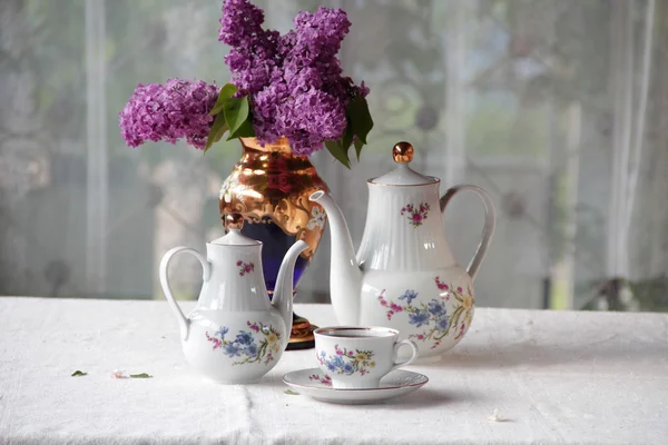 Tee in einer Tasse und ein fliederfarbener Strauß auf einem Tisch — Stockfoto