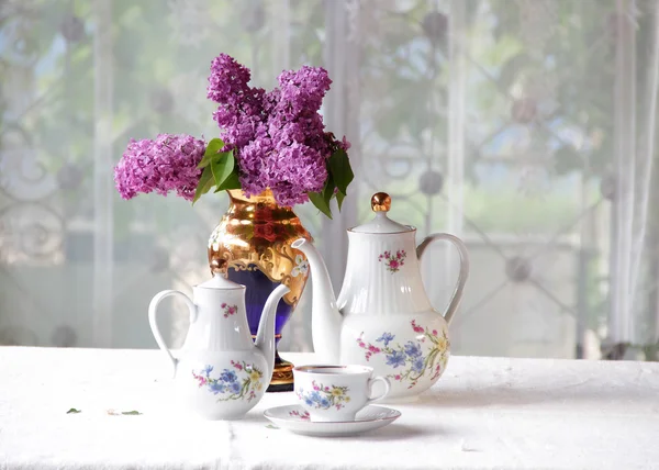 Tee in einer Tasse und ein fliederfarbener Strauß auf einem Tisch — Stockfoto