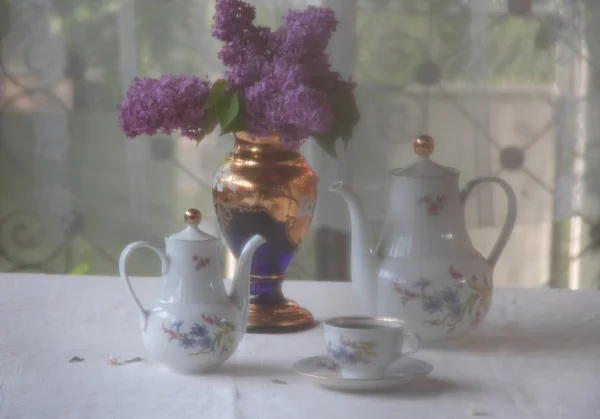 Tee in einer Tasse und ein fliederfarbener Strauß auf einem Tisch — Stockfoto