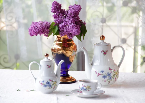 Té en una taza, y un ramo de lila en una mesa — Foto de Stock