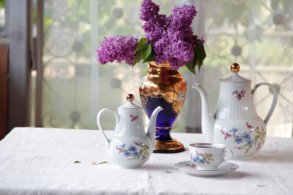 Tee in einer Tasse und ein fliederfarbener Strauß auf einem Tisch — Stockfoto