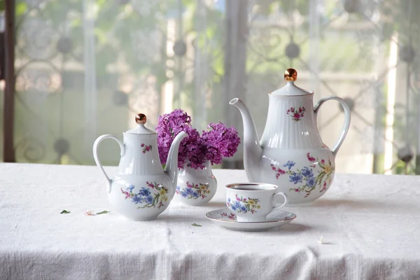 Tee in einer Tasse und ein fliederfarbener Strauß auf einem Tisch — Stockfoto