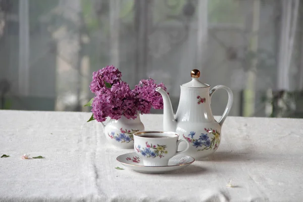Tee in einer Tasse und ein fliederfarbener Strauß auf einem Tisch — Stockfoto