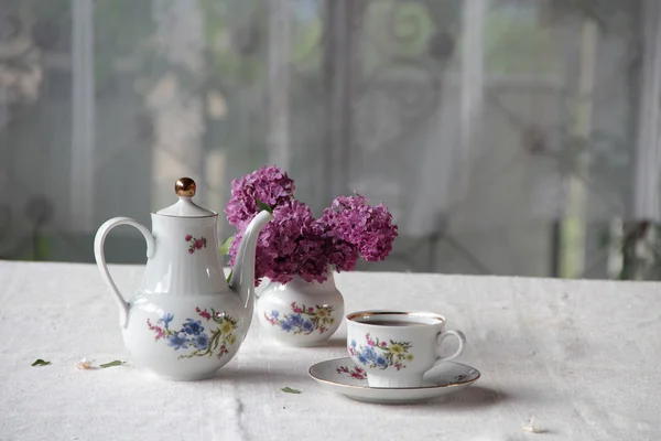 Tee in einer Tasse und ein fliederfarbener Strauß auf einem Tisch — Stockfoto