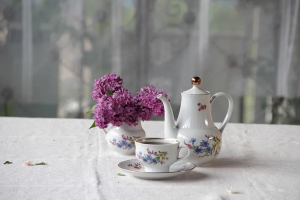 Tee in einer Tasse und ein fliederfarbener Strauß auf einem Tisch — Stockfoto