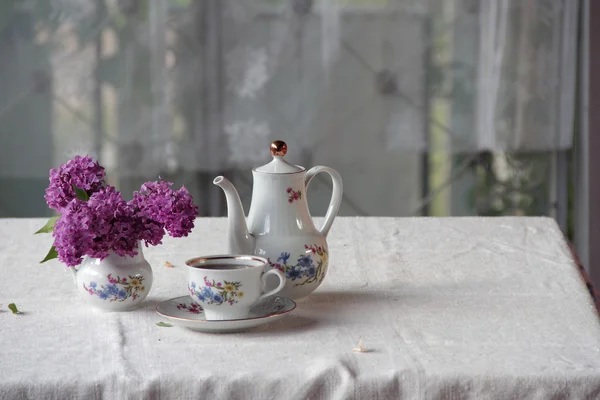 Tea in a cup, and a lilac bouquet on a table — Stock Photo, Image
