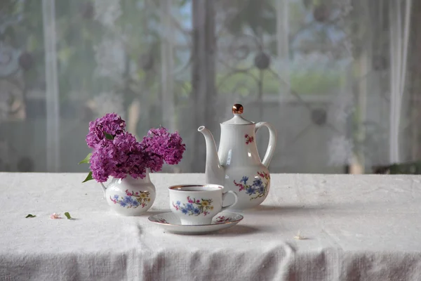 Tee in einer Tasse und ein fliederfarbener Strauß auf einem Tisch — Stockfoto