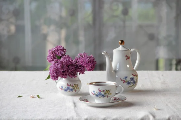 Tee in einer Tasse und ein fliederfarbener Strauß auf einem Tisch — Stockfoto