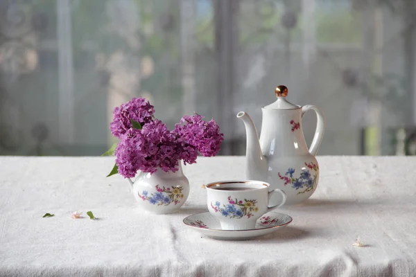 Tee in einer Tasse und ein fliederfarbener Strauß auf einem Tisch — Stockfoto