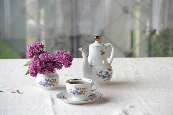 Tee in einer Tasse und ein fliederfarbener Strauß auf einem Tisch — Stockfoto