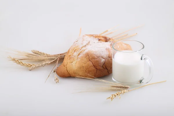 Milk in a transparent mug and a rich roll — Stock Photo, Image
