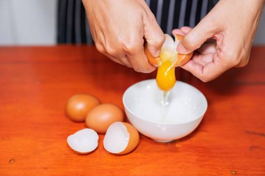 Bir kadın yemek pişirmek için ahşap masada seramik beyaz bir kaseye yumurta kırıyor.