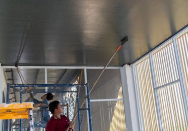 Adam duvarları ve tavanı gri renge boyuyor, ayakta duruyor..