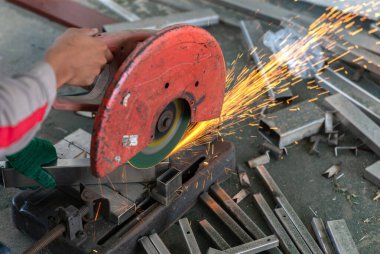 Erkek işçi, paslanmaz çelik dikdörtgen boruları kıvılcımlarla kesmek için fiber kesme makinesi kullanır.