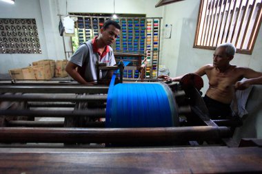 Yogyakarta, Endonezya, 3 Mart 2016. İki işçi hala geleneksel ekipman kullanan bir fabrikada örülmüş kumaşlar için temel malzemeyi döndürme işlemi yapıyor..