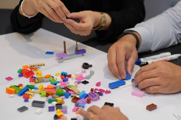 Close-up of hands of adults playing lego as a simulation of designing business strategy and human resource development.