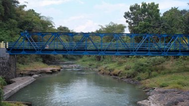 Derin bir derenin üzerindeki mavi çelik köprü. Köprü bir bağlantı yolu ya da geçiş olarak kullanılır.