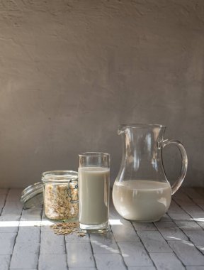 cam sürahi ve masada bir bardak yulaf sütü ve bir kavanoz yulaf ezmesi.